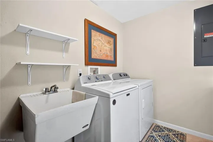 Dedicated utility space featuring a utility sink with dual-handle faucet, two wall-mounted storage shelves, and neutral wall paint