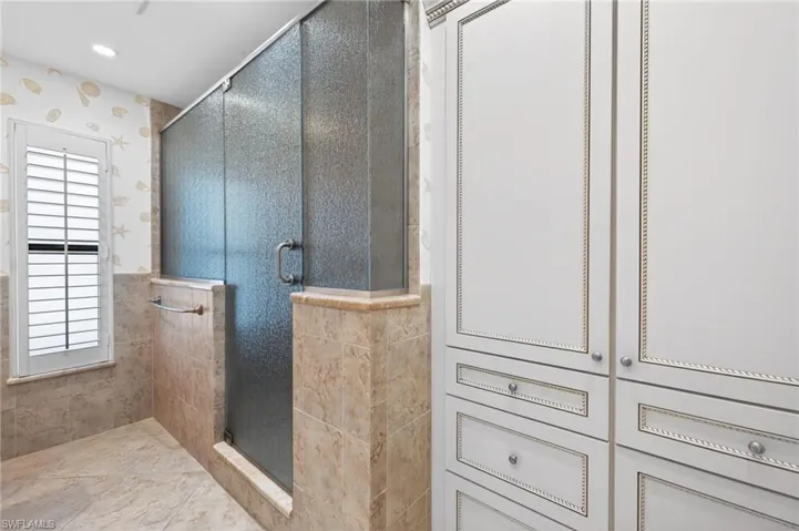 Frosted glass shower enclosure featuring a chrome handle, surrounded by stone-finish tile