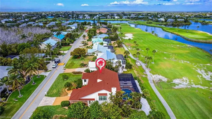 White exterior home with a red tile roof, featuring a screened-in pool area, lush green landscaping, and proximity to a golf course and water features