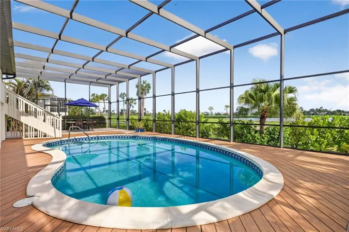 Screened outdoor living area featuring a freeform swimming pool with a tiled edge, surrounded by wood-finish decking