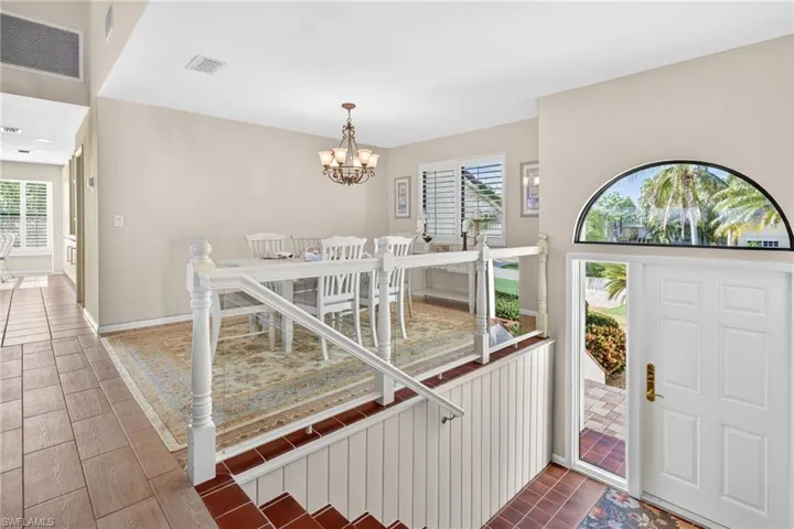 Entryway featuring a paneled white door with a semi-circular transom window, terracotta-style floor tiles, and a white balustrade with glass panels