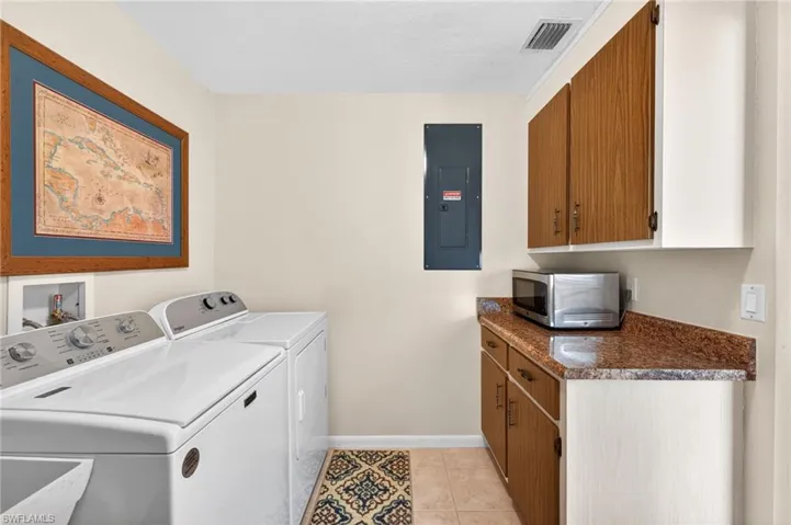 Dedicated utility area featuring a tile floor, wood-finish cabinetry, and a stone-look countertop