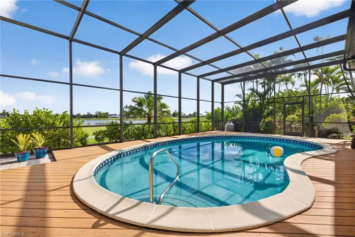 Screened pool enclosure featuring a kidney-shaped pool with a textured perimeter, surrounded by a wood-finish deck