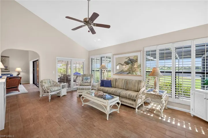 Spacious room featuring vaulted ceilings, wood-finish flooring, and multiple glass doors with plantation shutters
