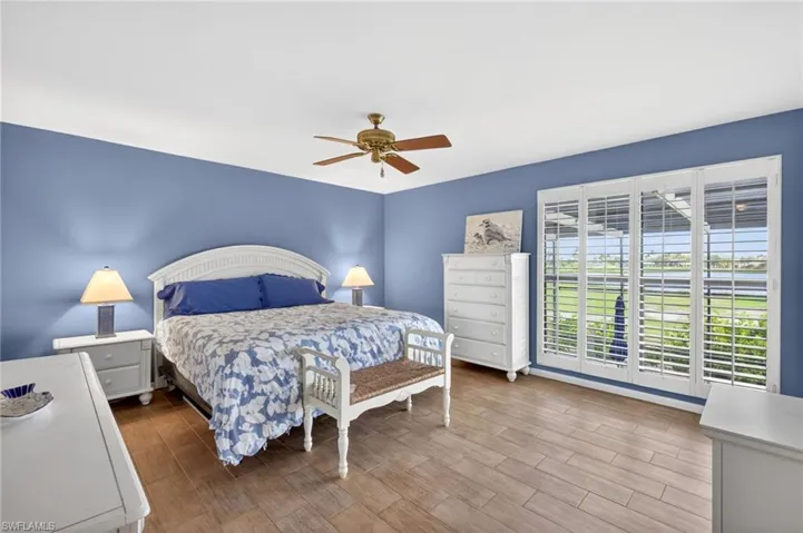 Wood-finish flooring throughout, featuring a ceiling fan with brass accents, and a wide window with white plantation shutters