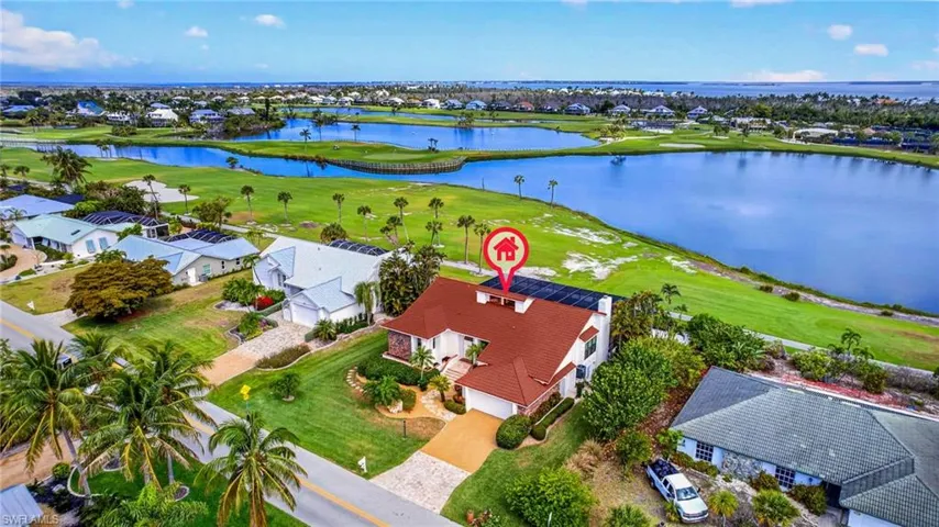 Waterfront property featuring a red tile roof, solar panels, a paved driveway, and mature landscaping