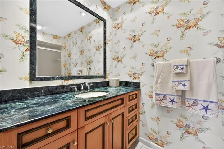 Bathroom featuring a wood-finish vanity with panel detailing, a dark green countertop, an undermount sink with a chrome faucet, and a large mirror framed in a matching dark green material
