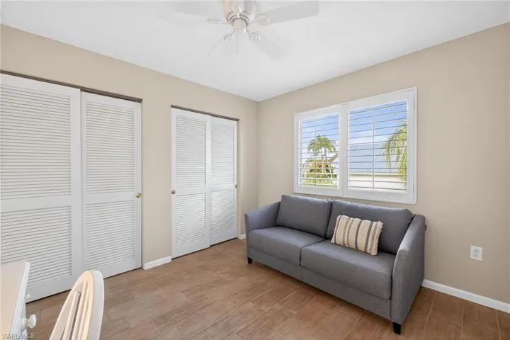 Room featuring wood-finish flooring, two sets of bi-fold louvered closet doors, a window with plantation shutters, and a ceiling fan