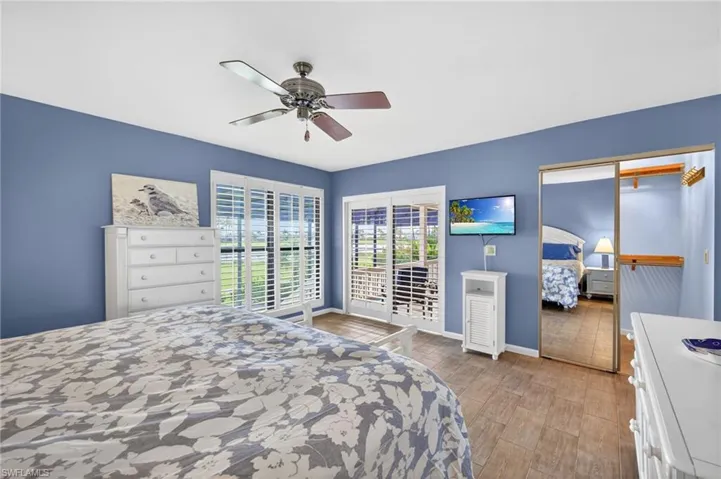 Bedroom featuring wood-finish flooring, a ceiling fan, and sliding glass doors with white plantation shutters opening to an exterior space
