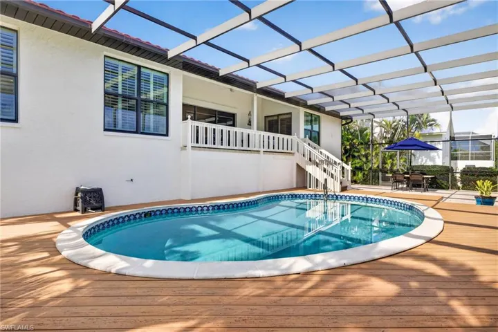 Outdoor entertainment space featuring a screened-in pool, wood-finish decking, white stucco exterior, second-story balcony with white railing, and a tile roof