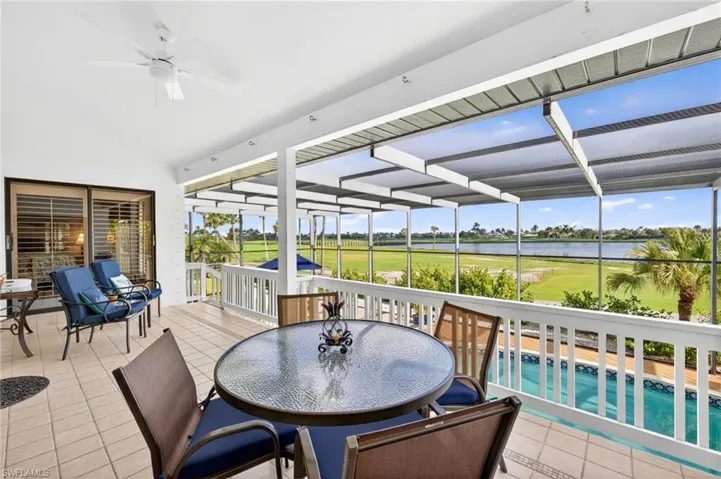 Expansive screened lanai featuring tiled flooring, a ceiling fan, sliding glass doors, a white railing, and a pool below, overlooking a golf course and water