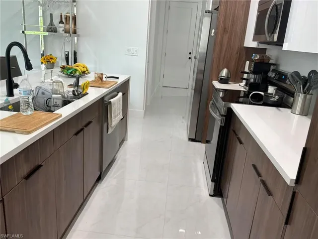 Modern kitchen featuring white countertops, wood-finish cabinetry, stainless steel appliances, and white tile flooring
