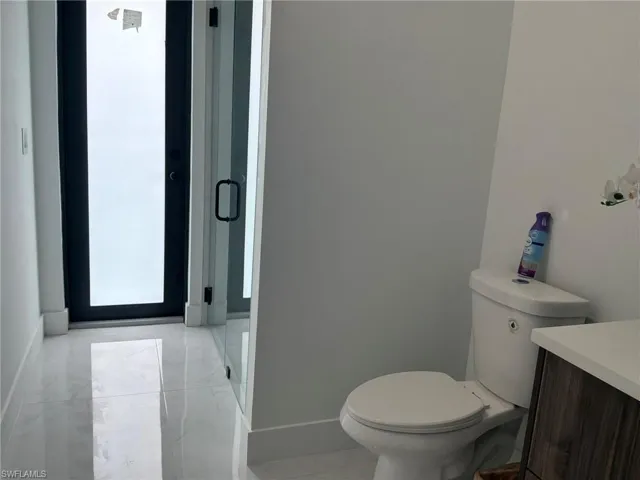 White tiled flooring throughout, a modern toilet, and a dark wood-finish vanity with a white countertop