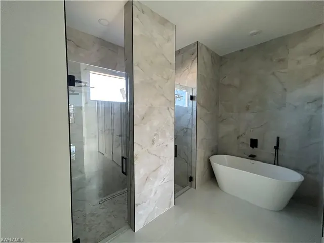 Full bathroom featuring a marble finish shower, a freestanding bath, and tile walls