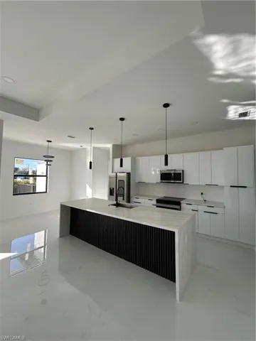 Kitchen with white cabinets, hanging light fixtures, a spacious island, light marble finish flooring, and light stone counters