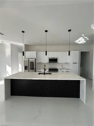Kitchen with white cabinetry, light stone countertops, a spacious island, fridge, and hanging light fixtures