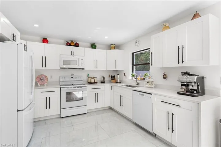 Kitchen with white cabinets, light countertops, white appliances, and a sink