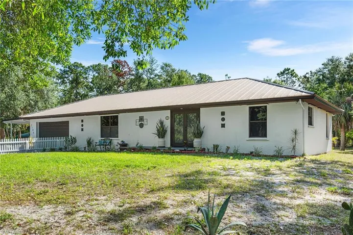 Ranch-style house with an attached garage, fence, a front yard, metal roof, and stucco siding