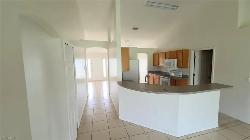 Kitchen with wood-finish cabinetry, white appliances, and a curved breakfast bar featuring a stone-finish countertop