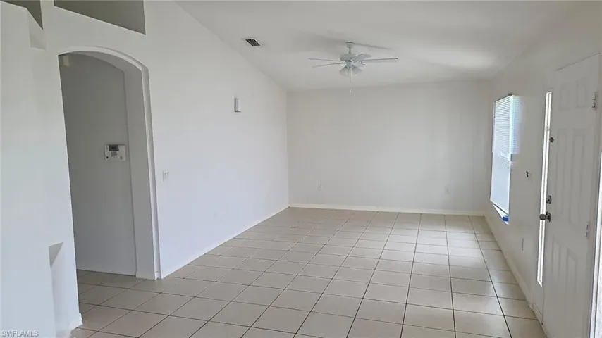 Spacious room featuring tile flooring, vaulted ceilings, and an arched doorway