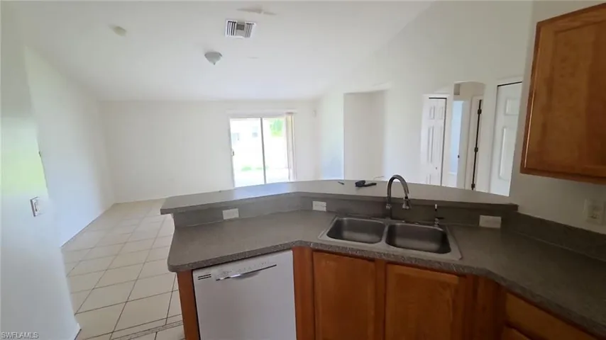 Kitchen featuring wood cabinetry, a double basin stainless steel sink with gooseneck faucet, a built-in dishwasher, and a breakfast bar countertop