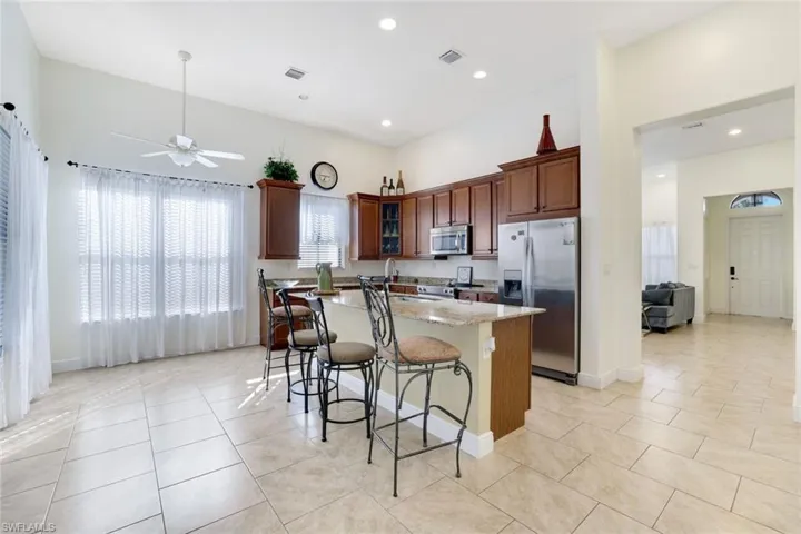 Kitchen with appliances with stainless steel finishes, light stone countertops, a breakfast bar area, glass insert cabinets, and a kitchen island with sink