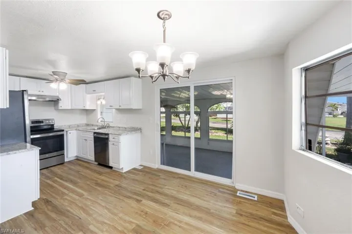 Kitchen with stainless steel appliances, a chandelier, light wood finished floors, and white cabinetry