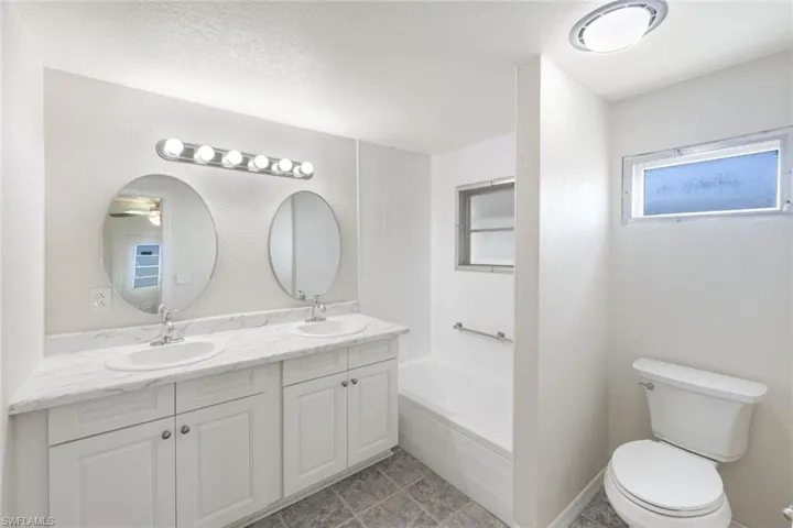 Full bathroom with double vanity, a textured wall, and a textured ceiling
