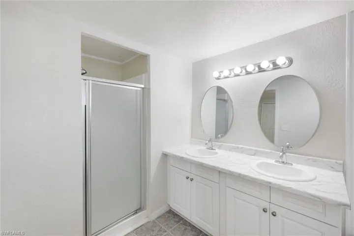 Bathroom featuring a shower stall, double vanity, a textured ceiling, and a textured wall