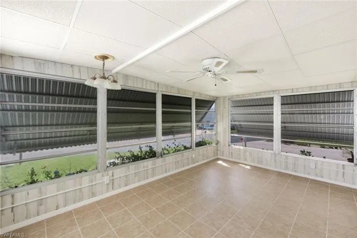 Unfurnished sunroom featuring ceiling fan, a drop ceiling, and tile patterned flooring