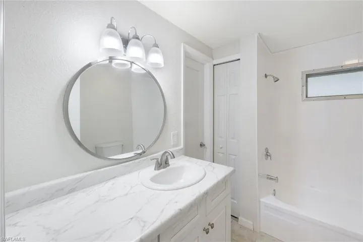 Bathroom with a closet, bathtub / shower combination, vanity, light tile patterned flooring, and a textured wall
