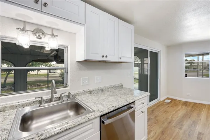 Kitchen featuring stainless steel dishwasher, light wood finished floors, white cabinets, a textured ceiling, and a textured wall