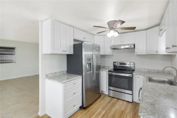 Kitchen with stainless steel appliances, light countertops, white cabinets, under cabinet range hood, and a textured ceiling