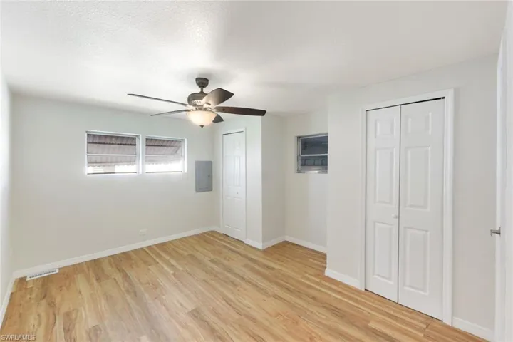 Unfurnished bedroom featuring two closets, light wood finished floors, ceiling fan, electric panel, and a textured ceiling
