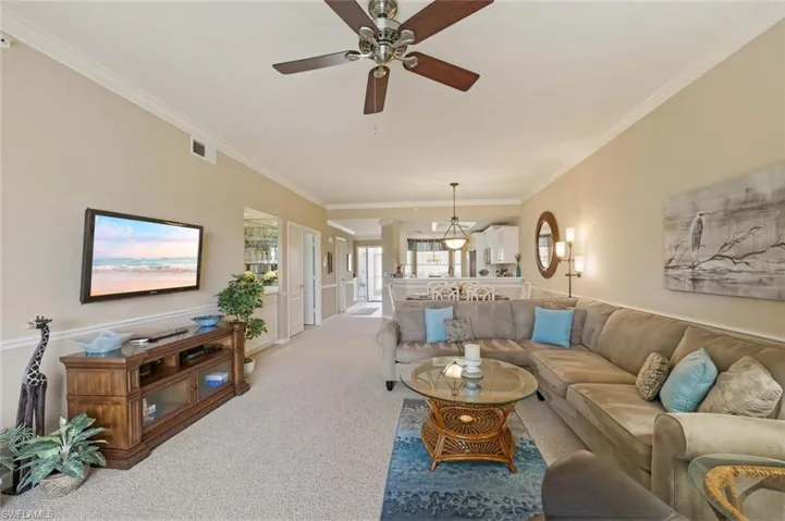 Living room with ornamental molding, carpet flooring, and ceiling fan