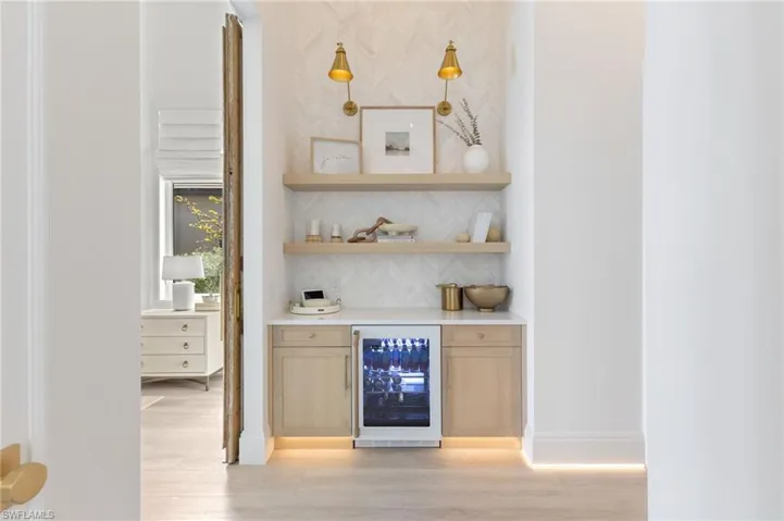 Indoor dry bar featuring beverage cooler, light wood finish cabinets, light stone countertops, open shelves, and light wood-style floors
