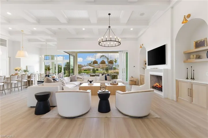 Living area featuring light wood-style floors, suspended lighting, a lit fireplace, coffered ceiling, and built in features