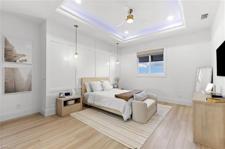 Bedroom featuring light wood finished floors, a raised ceiling, ceiling fan, and a decorative wall