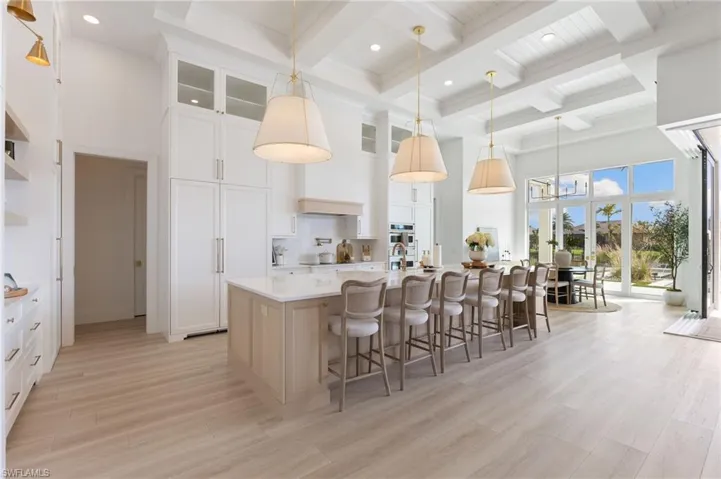 Kitchen featuring a breakfast bar area, a large island with sink, pendant lighting, coffered ceiling, and light wood-style flooring