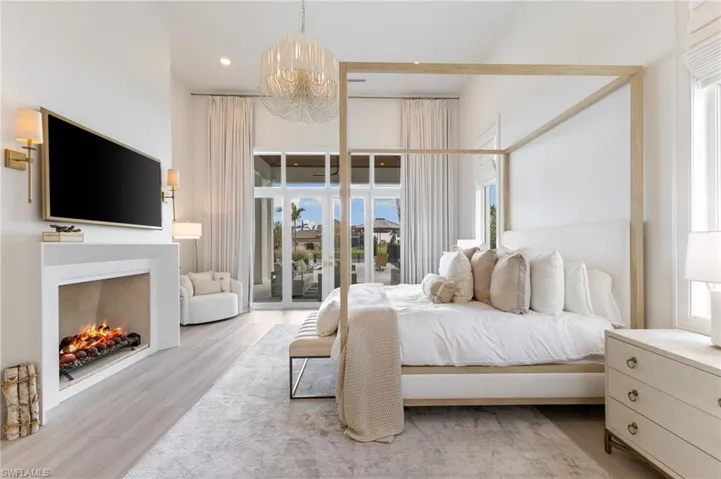 Bedroom featuring a lit fireplace, access to exterior, light wood finished floors, a chandelier, and a high ceiling