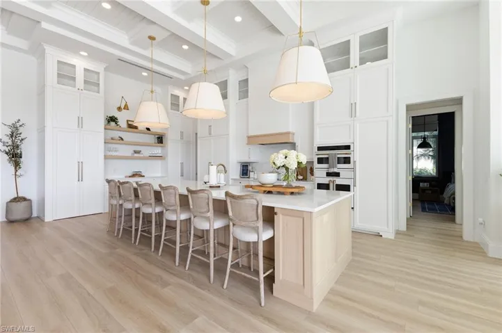 Two tone kitchen featuring open shelves, a breakfast bar area, light wood finished floors, glass fronted cabinets, and two tone color scheme