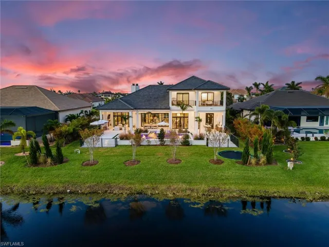 Back of house at dusk with a balcony, a water view, a patio, and a chimney