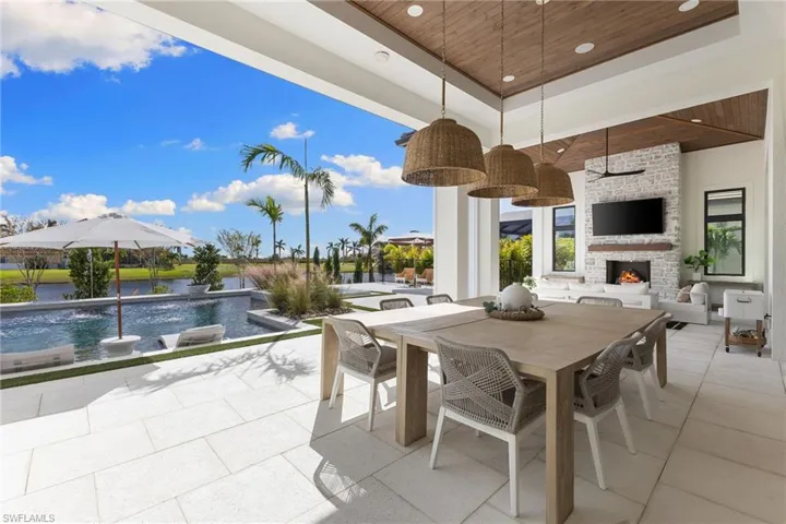 View of patio featuring a warm lit fireplace, outdoor dining area, an infinity pool, a water view, and a ceiling fan
