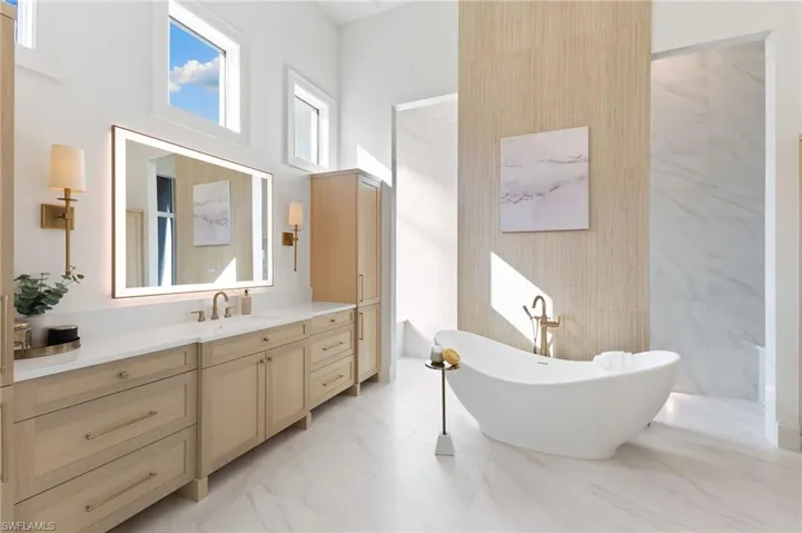Bathroom featuring vanity, a soaking tub, light marble finish floors, walk in shower, and a high ceiling