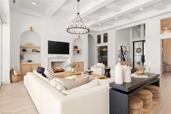 Living area featuring built in shelves, light wood-style floors, a lit fireplace, coffered ceiling, and hanging lights