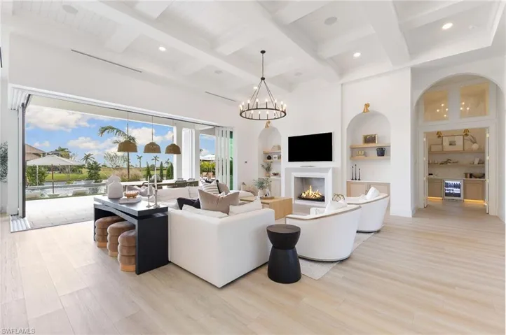 Living room featuring arched walkways, a warm lit fireplace, coffered ceiling, light wood finished floors, and built in features