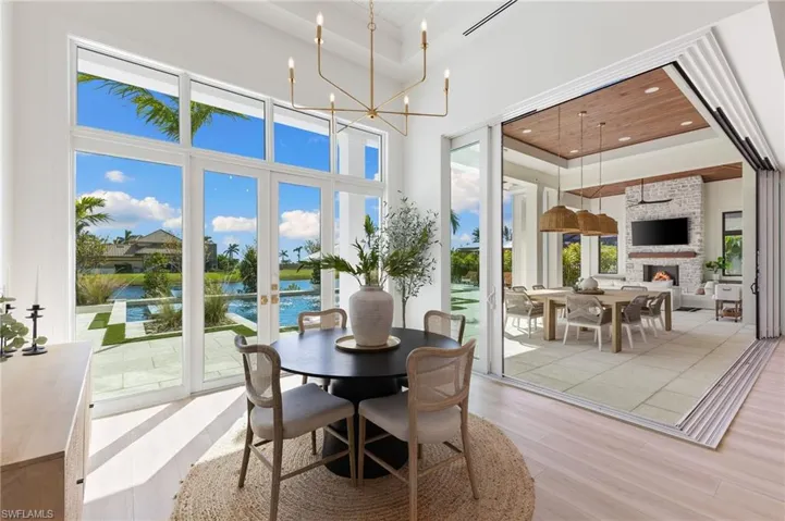 Dining area featuring light wood-style flooring, a high tray ceiling, hanging lights, french doors, and a large fireplace