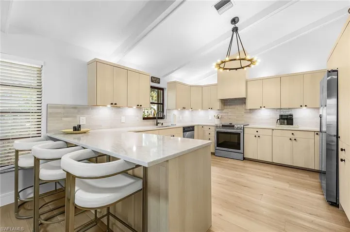 Kitchen with a peninsula bar, light wood style floors, vaulted ceiling with beams, stainless steel appliances, and tasteful backsplash