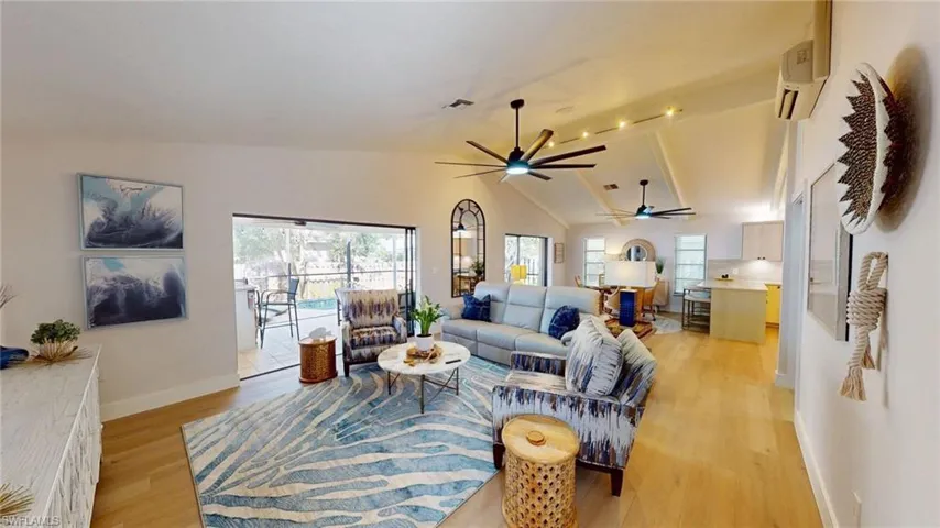Living area featuring vaulted ceiling, light wood-type flooring, healthy amount of natural light, and large ceiling fans