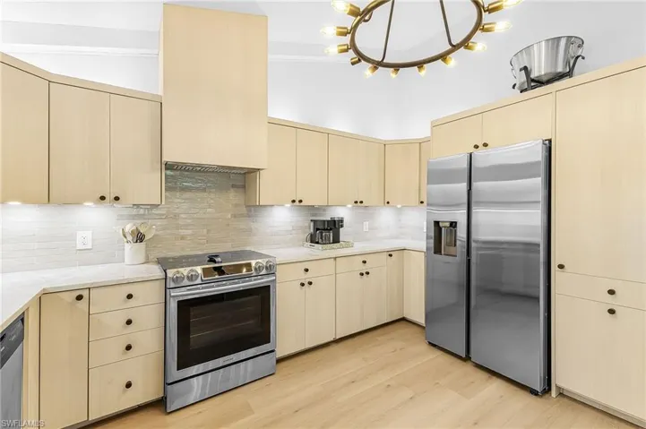 Kitchen featuring stainless steel appliances, tasteful backsplash, Taj Mahal quartz counters, and light wood style flooring & modern  cabinetry